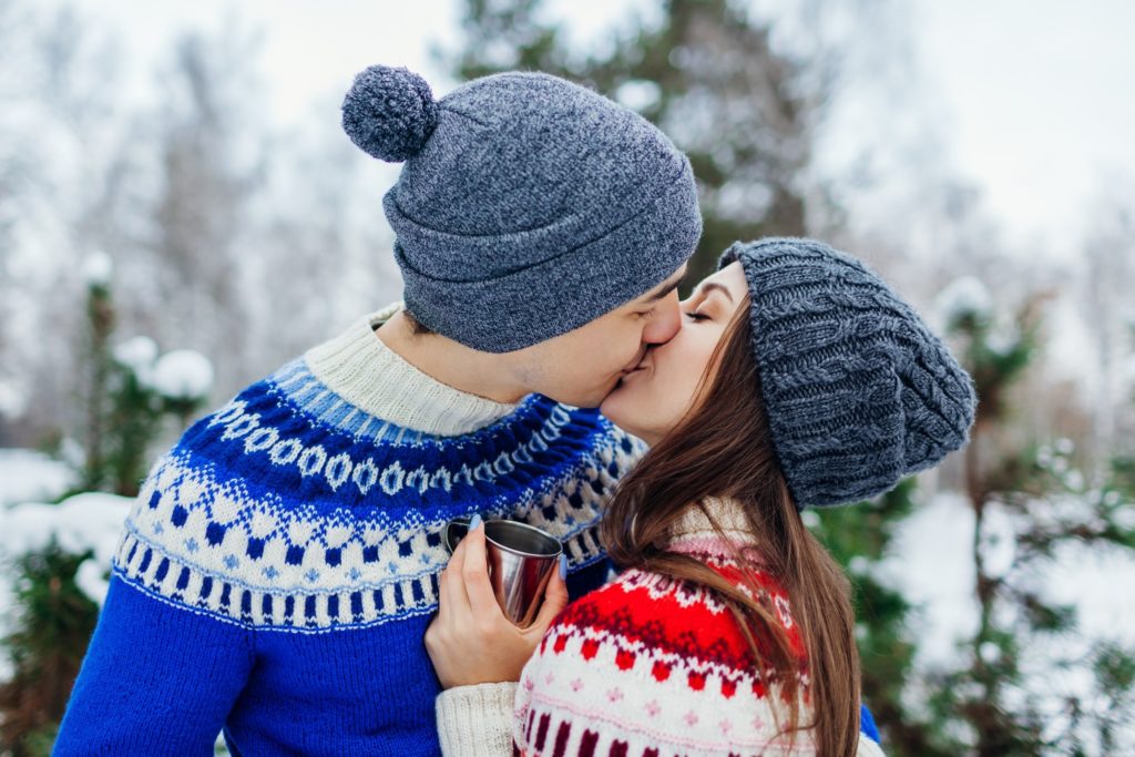 Couple in holiday sweaters kissing in the snow